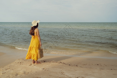 穿着黄色衣服的女人站在海边风吹的图片