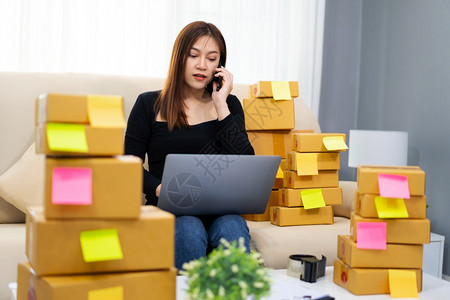女企业家在智能电话上讲使用笔记本电脑在家庭办公室网上销售产品中小型企业务图片