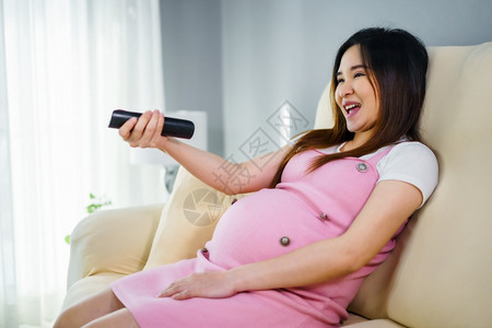 在客厅沙发上用遥控器观看电视的孕妇图片