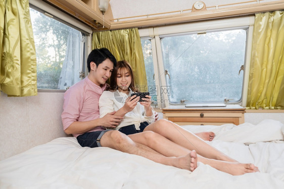 年轻夫妇在野营车RV面包汽旅馆的床上使用智能手机图片