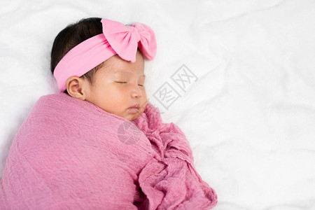 新生婴儿睡在床上的粉色布织毯子中图片