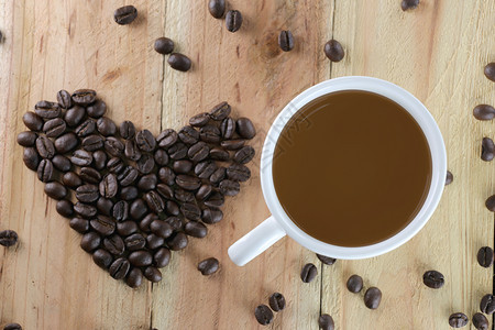 白咖啡杯和豆是木材背景的心脏形状图片