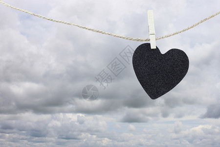 黑心纸挂在雨云背景的棕色黄绳上关于爱和心碎的观念图片