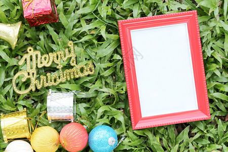 在绿草坪上的圣诞装饰品上面有圣诞快乐的金条地板上有红色的空木框图片