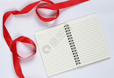 红丝带和白色背景上的空笔记本用于设计您的工作概念图片