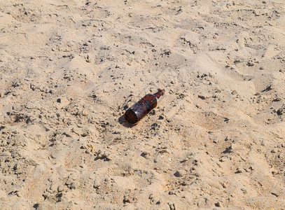 一瓶空啤酒躺在沙子上图片