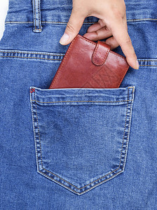 蓝色牛仔裤后口袋的棕色皮包和人手把它拔出来一个完整的框架图片