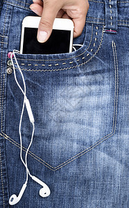 人手在蓝色牛仔裤前口袋装上耳机的白色智能手关上图片