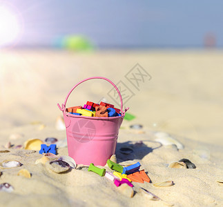 粉红的婴儿铁桶满的木质多彩字母站在沙子上关图片