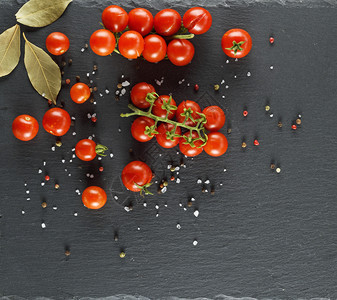 树枝上的红樱桃番茄洒满盐和胡椒黑色石墨背景图片