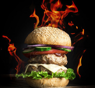 大汉堡包配两个油炸切饼奶酪和蔬菜在燃烧的火焰中用圆面粉包图片