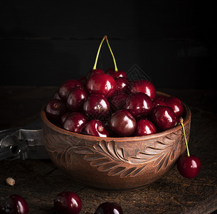 成熟的红多汁甜樱桃在木制桌子上的棕土碗里图片
