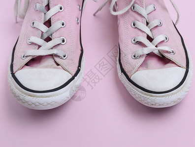 一对穿旧的粉红色运动鞋背景上有白鞋带关上图片