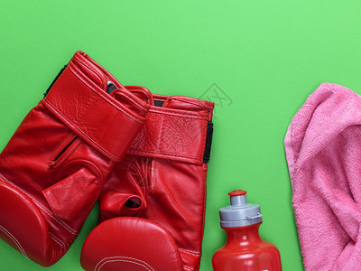 红色皮拳击手套塑料水瓶和粉红色毛巾绿背景顶部空背景图片
