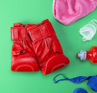 红色皮拳击手套塑料水瓶粉红色毛巾和绿背景的蓝纺织品绷带图片