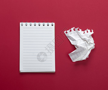 张开笔记本上面有白的床单和一块碎纸在红色背景的纸上撕扯出来图片