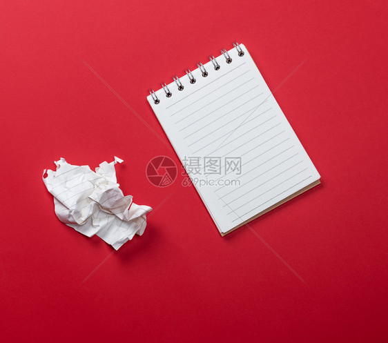 张开笔记本上面有白的床单和一块碎纸在红色背景的纸上撕扯出来图片