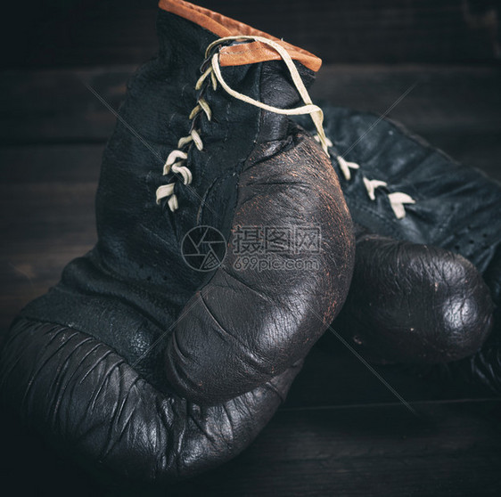 一对非常老旧的黑色皮革拳击手套在棕色木制背景上图片