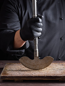 黑衣厨师手里握着一把用于肉类和蔬菜的金属老刀图片