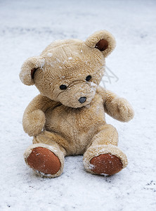 老泰迪熊坐在白雪上冬天图片