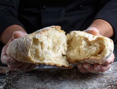 厨师手握着新鲜烤白面粉包的一半图片