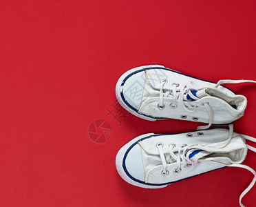 一对白色的旧式纺织运动鞋上面的红色背景是的顶面视图上有不松开的鞋带图片
