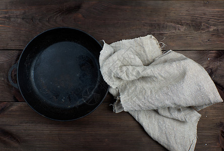 黑色圆煎锅顶视图在棕色木制桌子上用柄和灰色的餐巾纸在棕木制桌子上图片