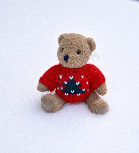 穿着红色毛衣的小泰迪熊独自坐在白雪中图片