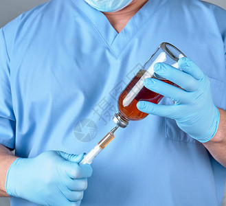穿蓝制服的医生拿着注射针筒和装有剂的玻璃瓶关上图片