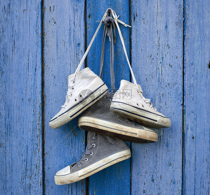 两对非常古老的纺织运动鞋挂在钉子上旧蓝色木头背景上图片