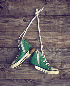 一对旧的绿色纺织运动鞋从带子上挂在灰色木壁复制空间图片