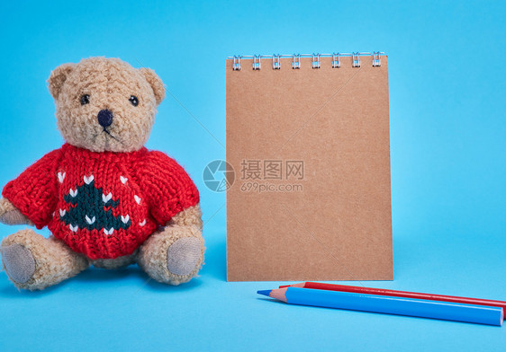 蓝色背景的棕白螺旋笔纸上面有棕色页纸铅笔和棕色小泰迪熊图片