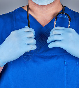 穿着蓝色制服和旧乳胶手套的医生脖子上戴着黑色听诊器关上图片