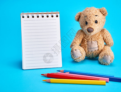 小棕色泰迪熊和蓝背景的空白笔记本图片