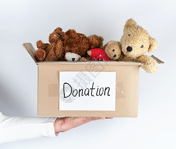 男手拿着纸面棕色盒子带着儿童玩具熊白色背景慈善概念图片