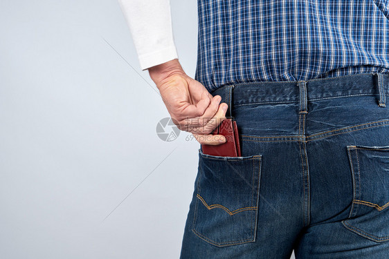 穿蓝色牛仔裤的男人和一身格子衬衫将皮棕钱包塞进裤子后口袋白色背景复制空间图片