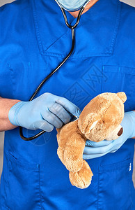 蓝制服医生和戴棕色泰迪熊的乳胶手套儿科医生治疗玩具图片