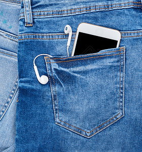 在蓝牛仔裤后口袋里有耳机的白智能手关上图片