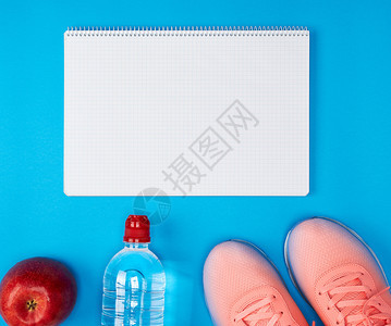 开放的空笔记本和运动妇女健身服装顶视蓝背景图片