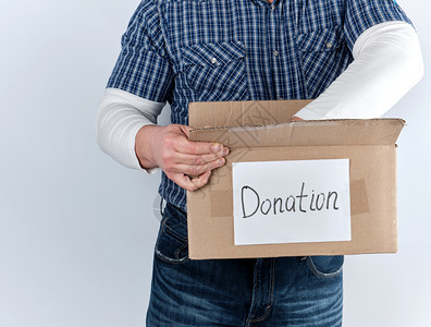 穿蓝格衬衫和牛仔裤的男人拿着一个大棕色纸盒上面写着赠品帮助有需要的人概念白种背景图片