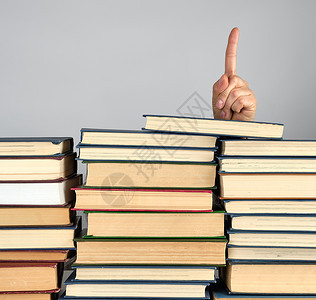 灰色背景上不同书堆的叠一只手从的后面刺出来并显示食指注意符号图片