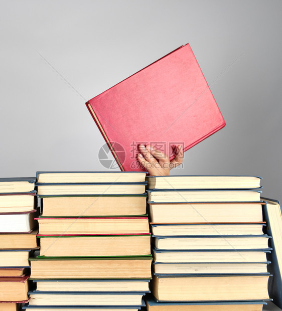 灰色背景上不同的书堆手持有一本红色硬封面的书图片