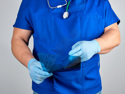 蓝制服医生和无菌乳胶手套持有和检查灰底腿骨X光图片