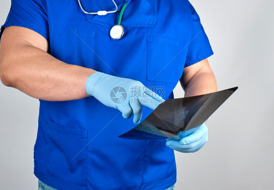 蓝制服医生和无菌乳胶手套持有并检查灰底X光X图片