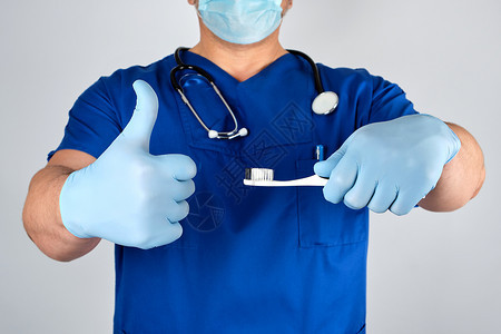 持有牙刷口腔卫生概念的无菌乳胶手套和蓝色制服的医生图片