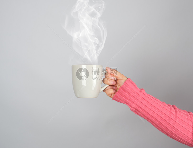 女人手上的灰色陶瓷杯子白蒸汽从里冒出来灰色背景图片