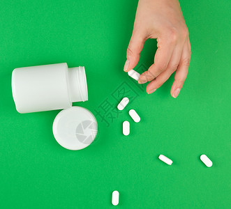 白塑料罐头和分散在绿色背景的叶子药片该妇女手握一粒药片背景图片