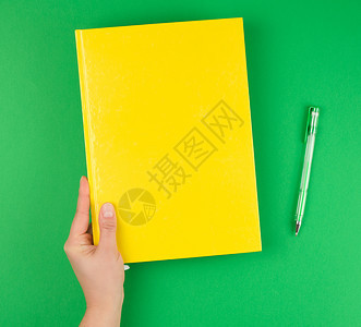 女手握黄色封闭笔记本和绿色背景顶视图图片