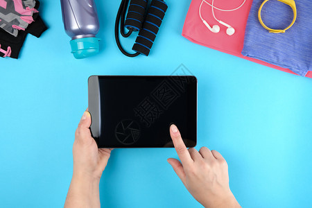 女手握电子平板空白黑屏旁边是健身衣蓝背景顶视图图片
