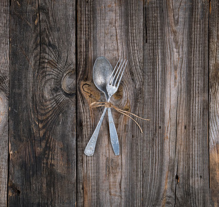 旧金属叉子和勺用棕色绳捆绑在灰木制桌板上图片